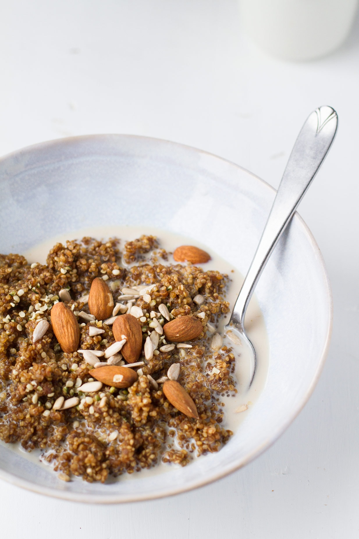 A blue bowl with breakfast quinoa and milk, topped with sunflower seeds and almonds.