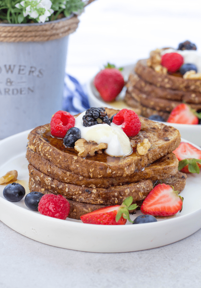 A stack of whole wheat bread french toast, topped with cream and berries.