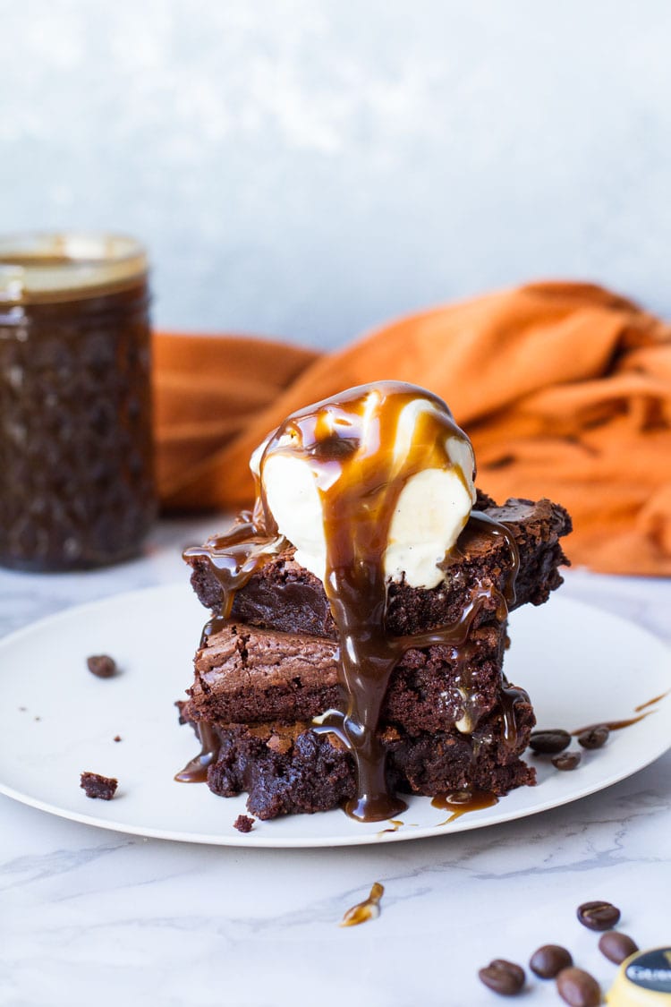Three Guinness caramel brownies squares stacked, melting ice cream scoop on top with a lot of caramel sauce.