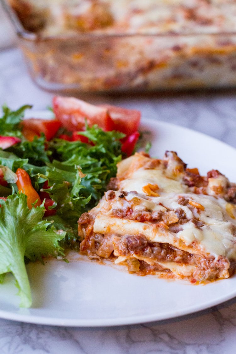 Lasagna and side salad on a white plate.