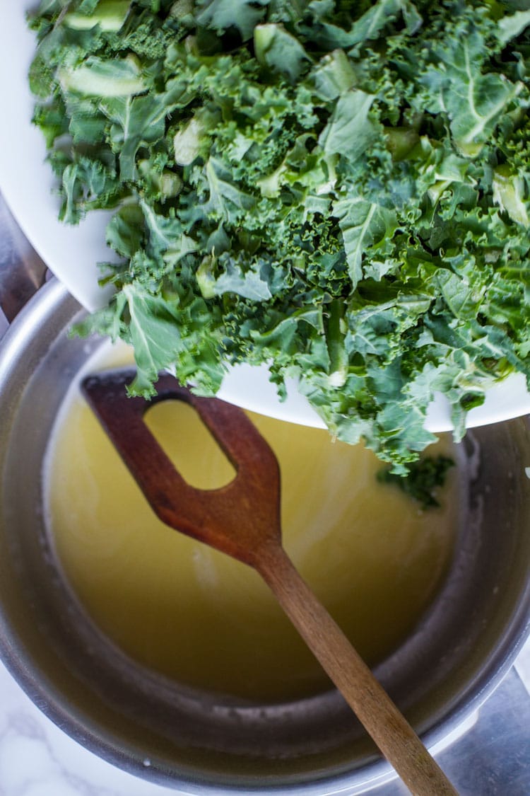 Adding chopped kale to melted butter in a saucepan.