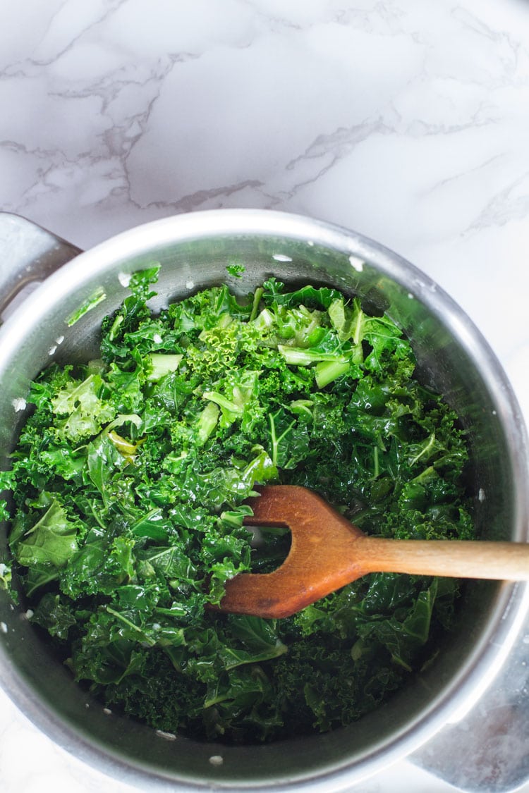 A casserole with wilted kale and a wooden spatula.