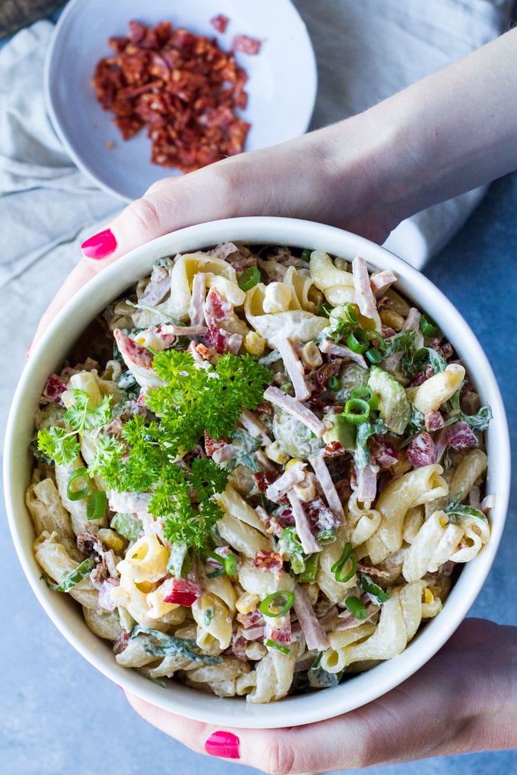 Hands holding a big serving bowl with creamy pasta salad.