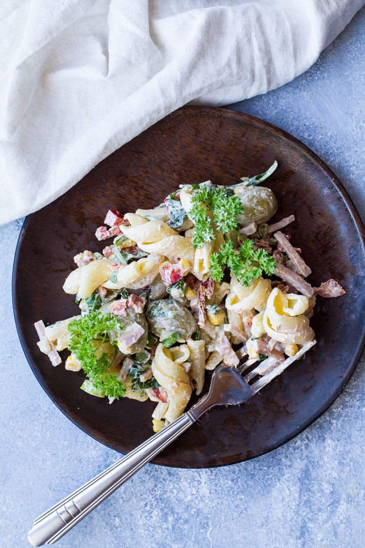 One serving of creamy pasta salad on a wooden plate.