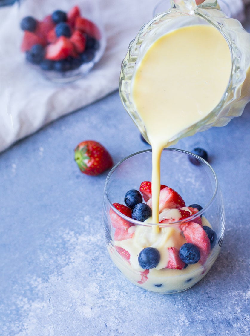 Pouring custard sauce over fresh berries in a glass.