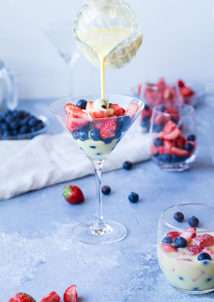 Pouring crème anglaise in a martini glass filled with strawberries and blueberries.