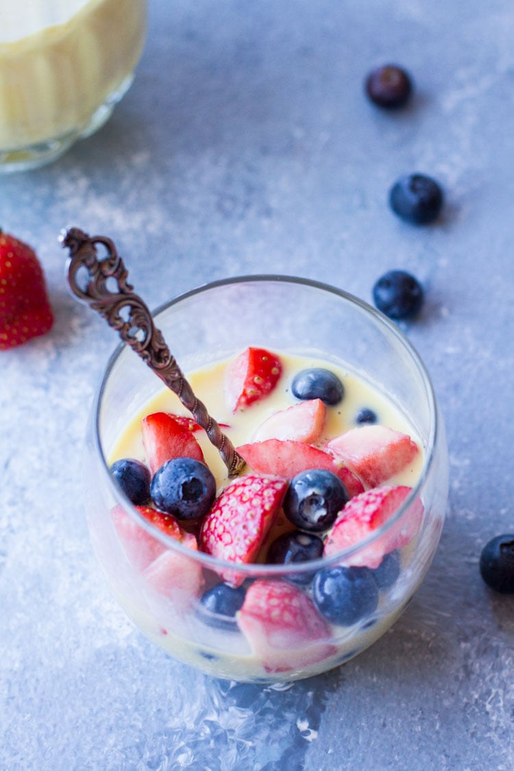 Glass with vintage spoon, fresh berries and creme anglaise. Blue background.