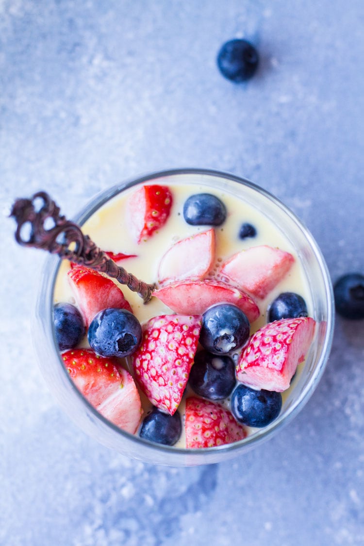 Glass filled with fresh strawberries and blueberries, topped with vanilla custard sauce. Flatlay.