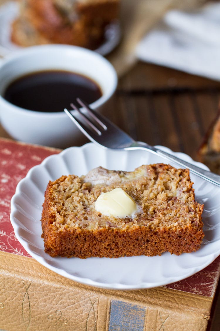 Slice of banana bread with a dollop of butter, coffee in the background.