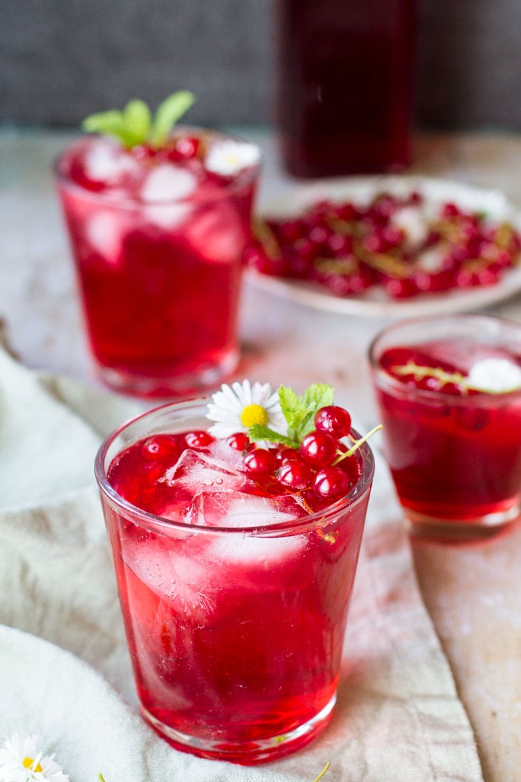 Three glasses with berry cordial, garnished with mint leaves and red currants.