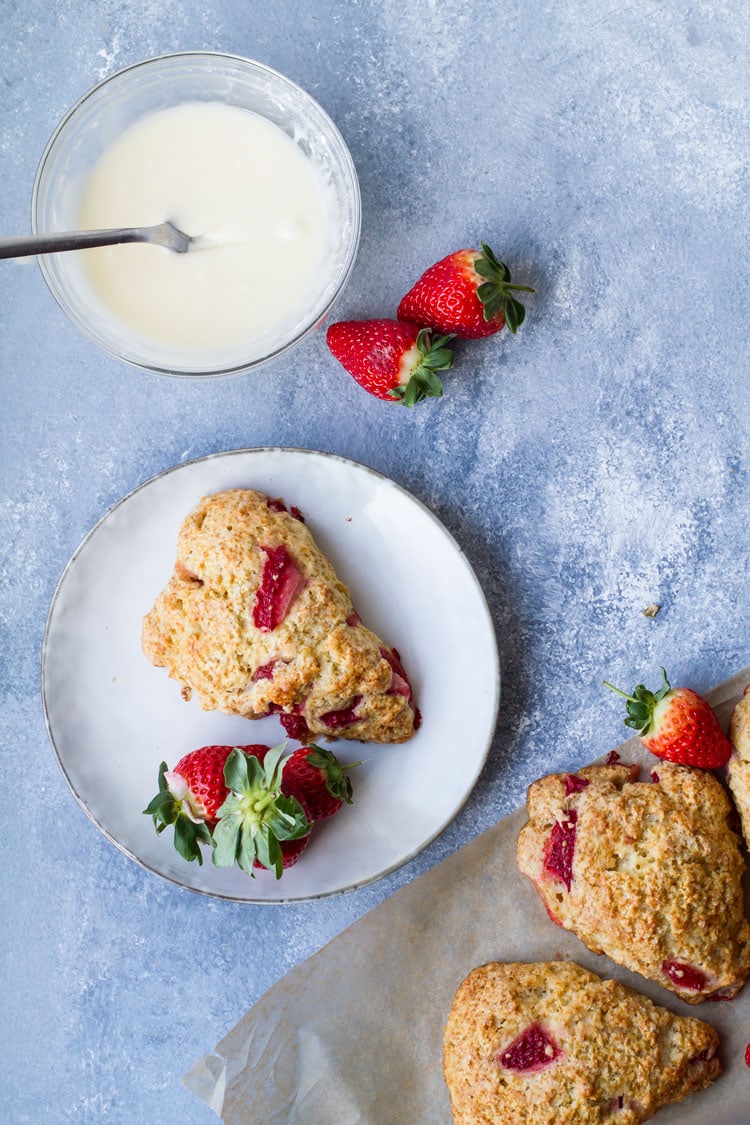One scone on a plate, strawberries scattered around.