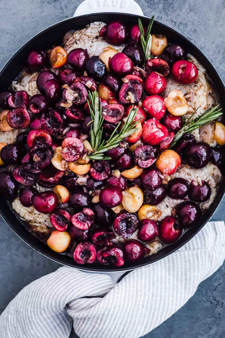 Large skillet with chicken and fresh cherries.