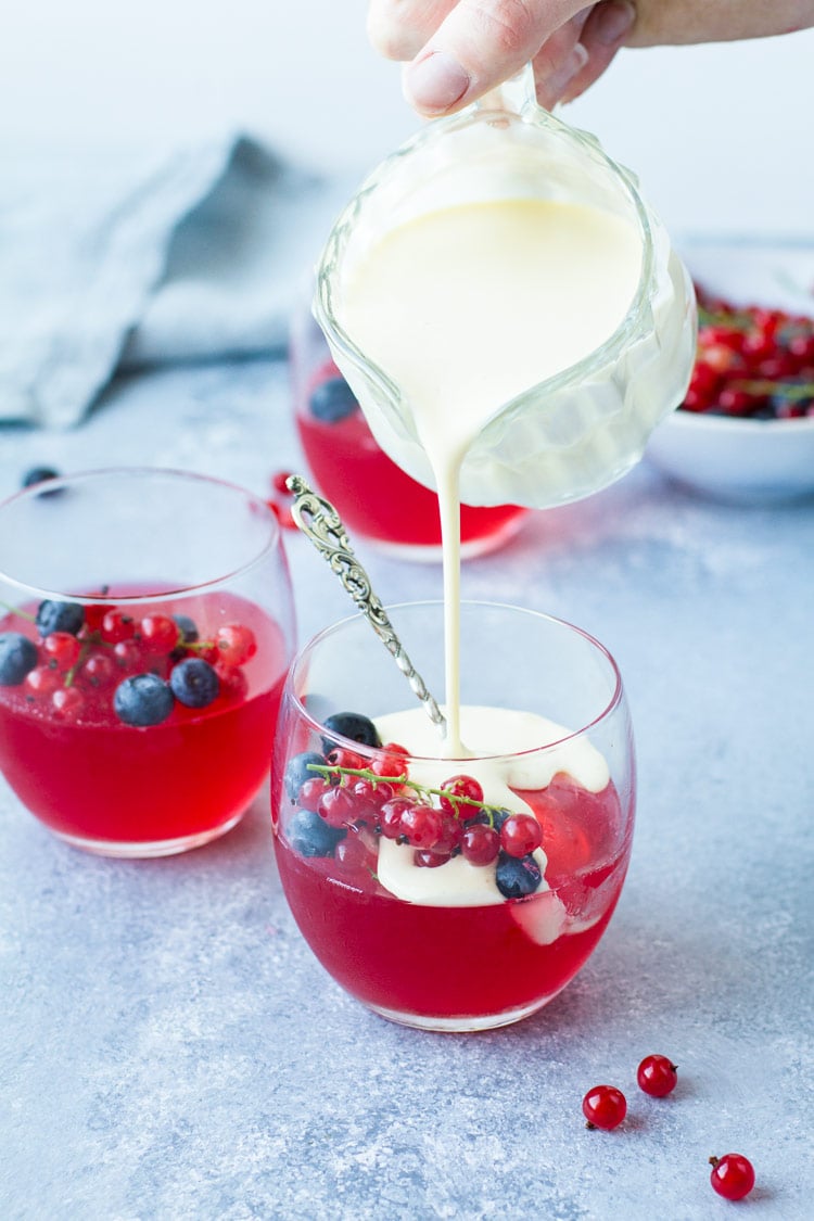 Pouring créme anglaise into a glass of jello and fresh berries.