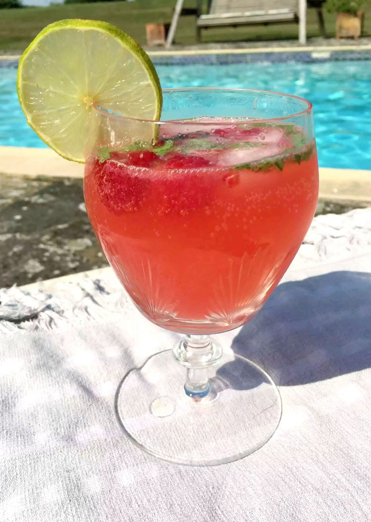 Large cocktail glass with raspberry cooler and lime slice. Pool in the background.