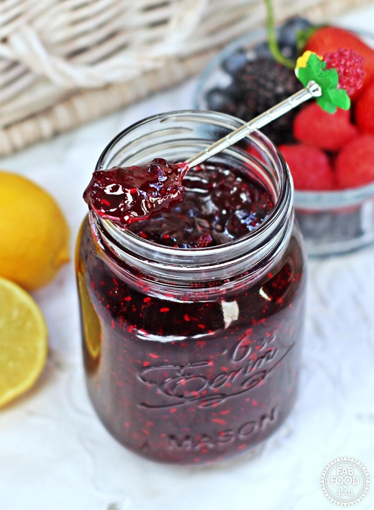 Mason jar with dark jam, a spoon with jam on top.
