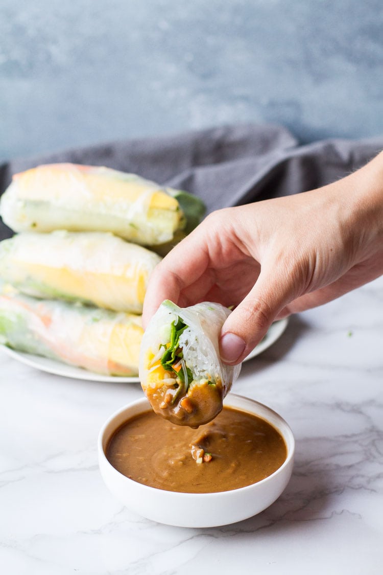 Hand holding a sliced open summer roll dipped in peanut sauce. 