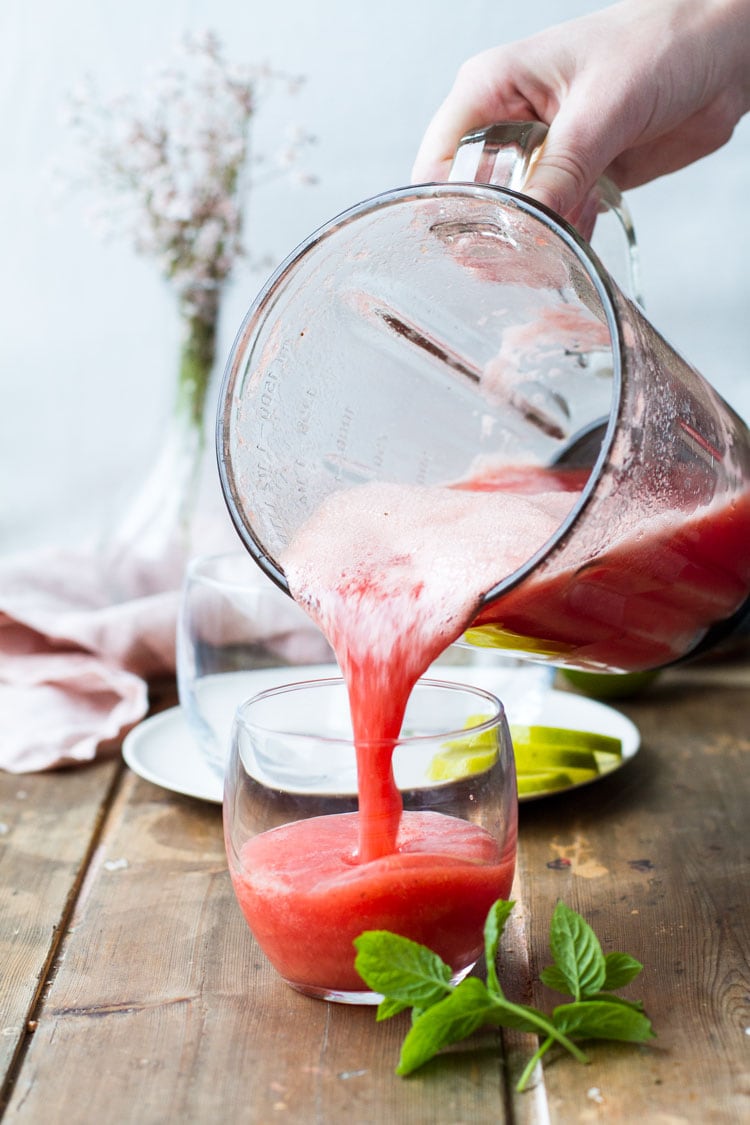 Pouring watermelon limeade from a blender into a glass.