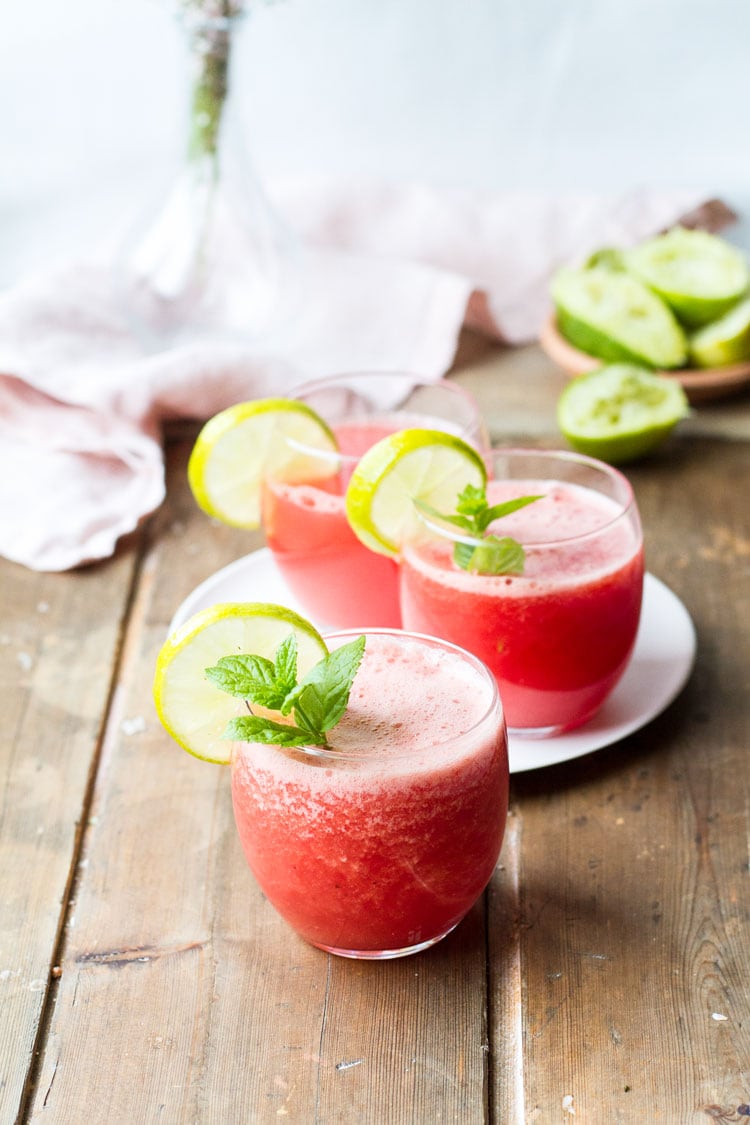 Three glasses with watermelon drink, mint garnish and lime wedges.