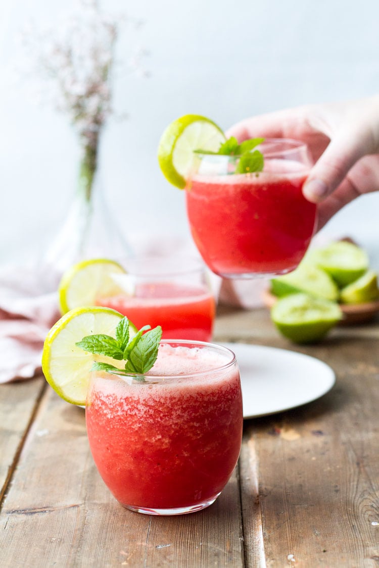 Three glasses with watermelon drink, hand holding one of the glasses.