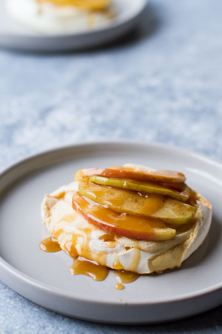 One mini pavlova with sliced apples and drizzles of caramel sauce.