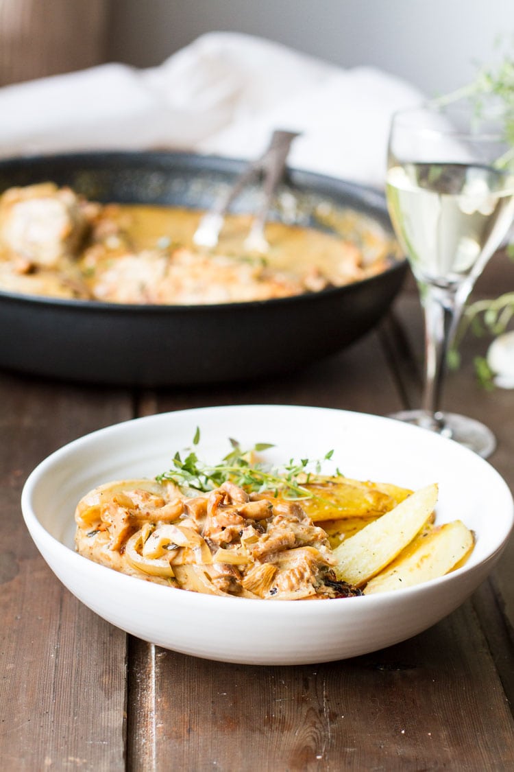 White bowl with chicken breast and cream sauce. White wine on the side.