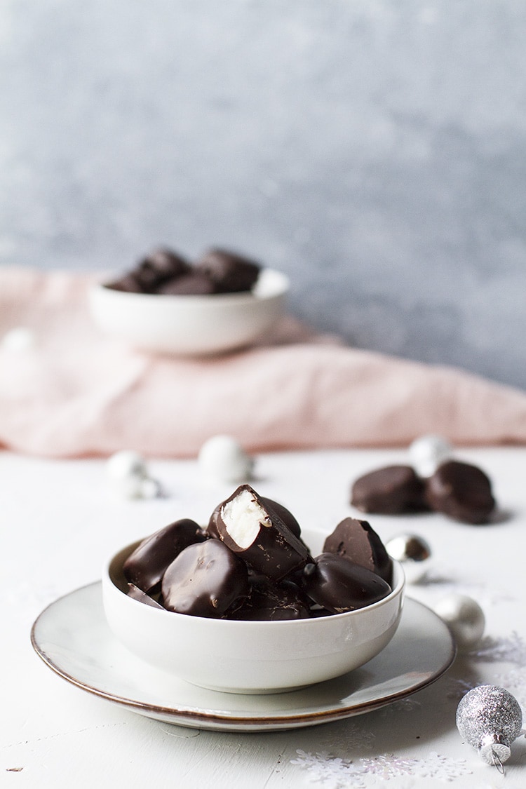 Peppermint patties in a small white bowl on a plate. Pink linen in the background.