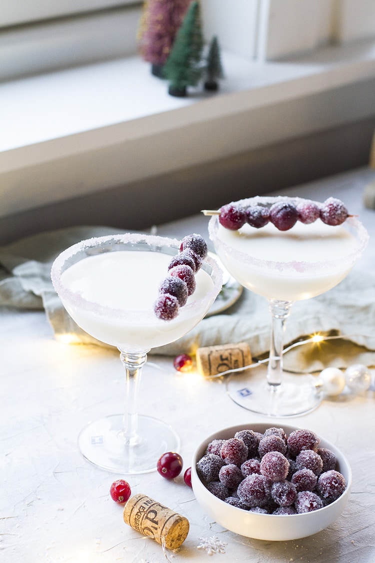 Two coupé glass with a white cocktail and sugar cranberries garnish.